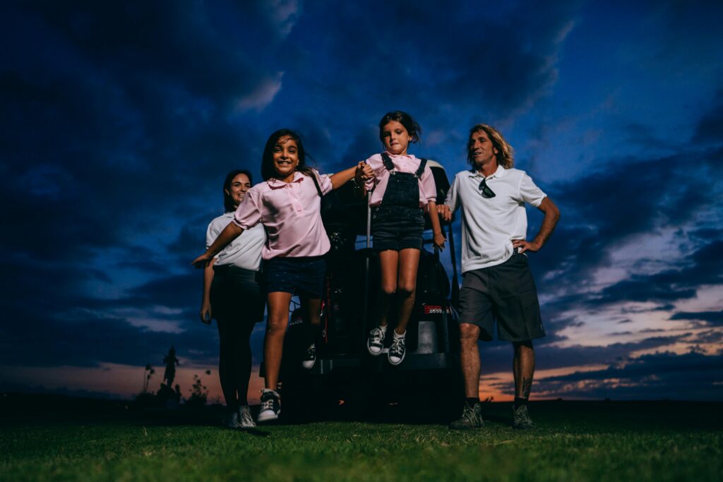 A happy family with kids having fun near a golf cart at sunset.