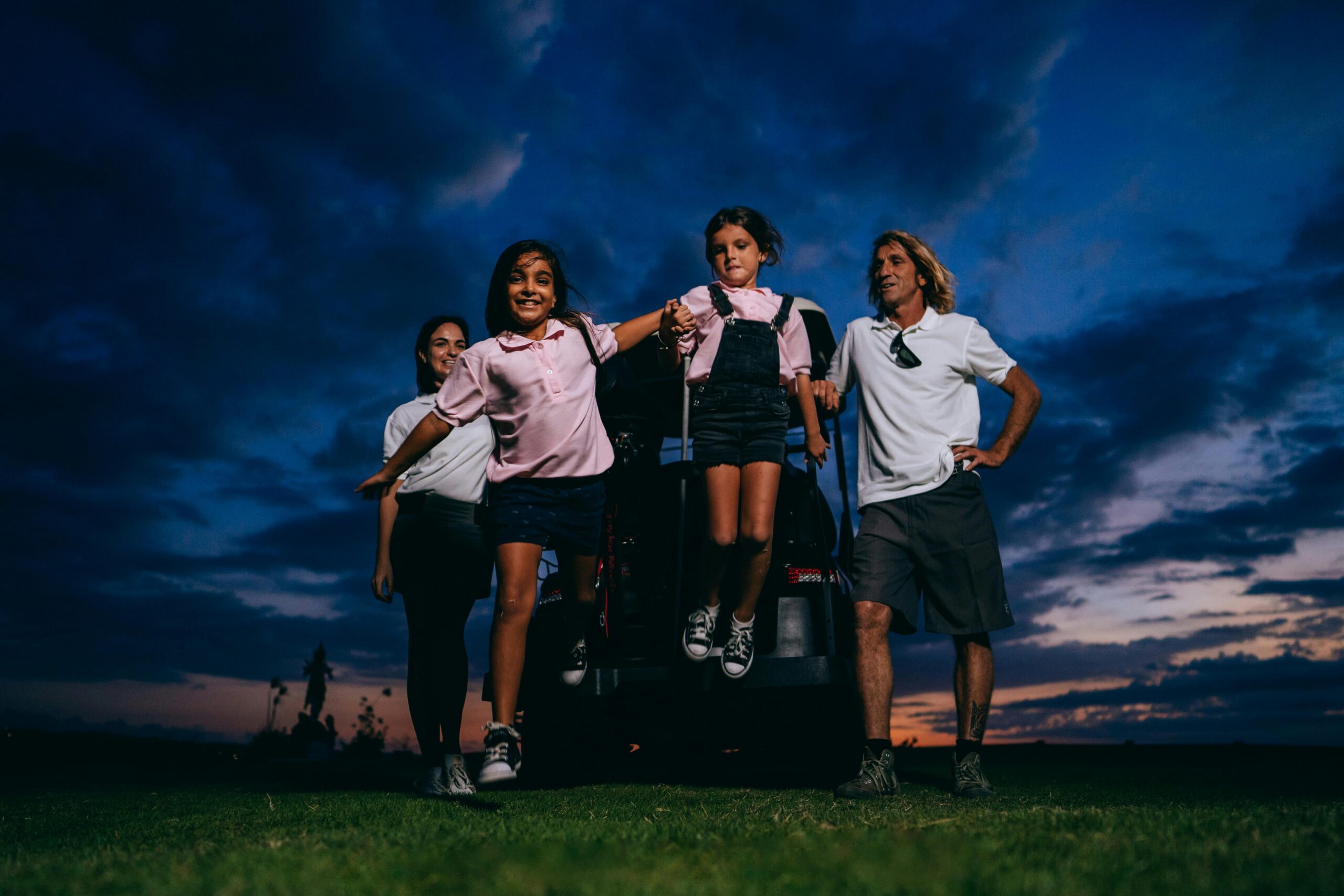 A happy family with kids having fun near a golf cart at sunset.